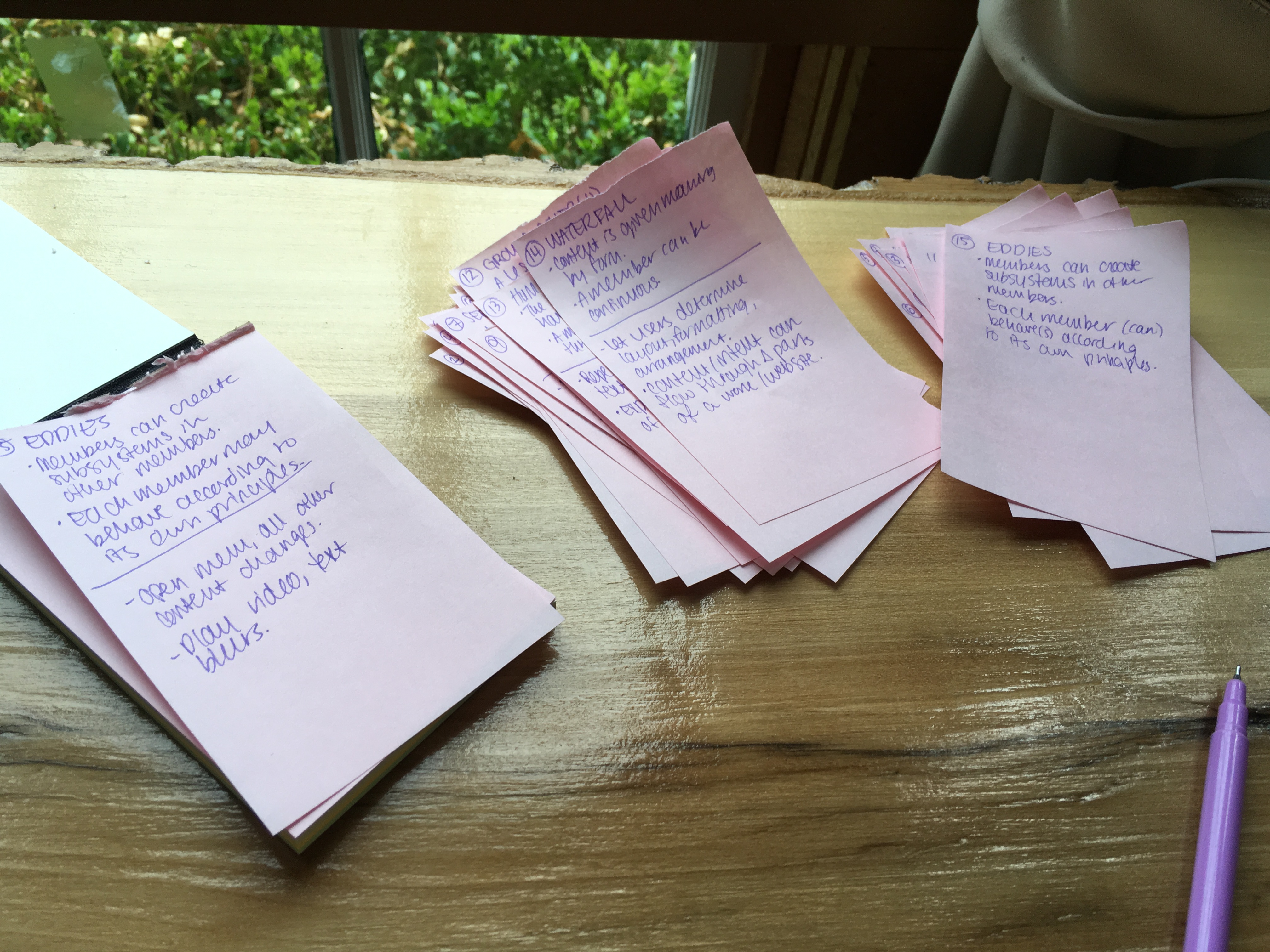 Three thick stacks of pink sticky notes on a wooden table in front of a window.